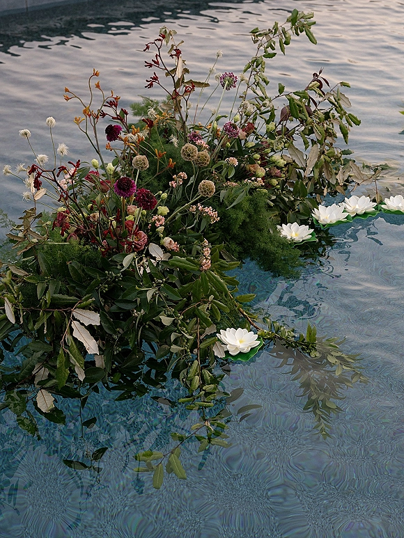 Floating floral arrangement with a floating greenery garland and wildflowers, dotted with water lily floats on shimmering pool water