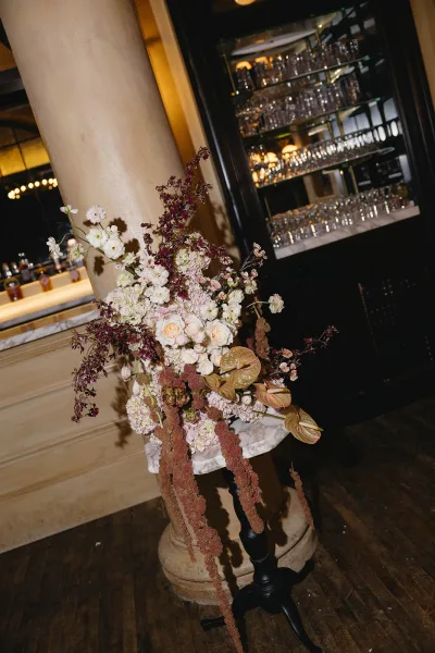 Wedding floral arrangement styled as a pedestal flower arrangement with glossy anthurium, set against bar shelves and glassware.