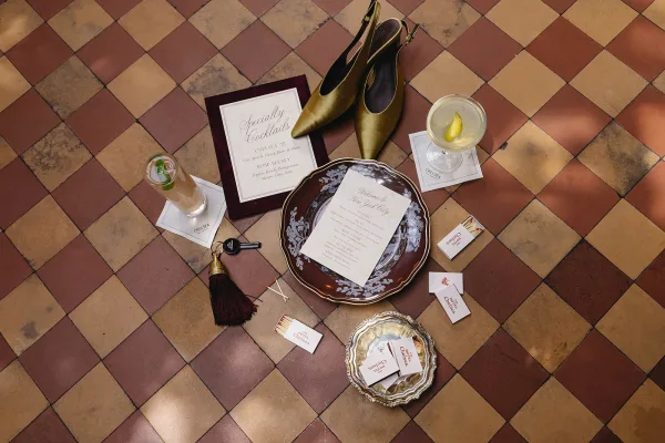 Invitation suite styled as a wedding flat lay, elegantly arranged beside bridal shoes on a distinctive checkered tile floor.