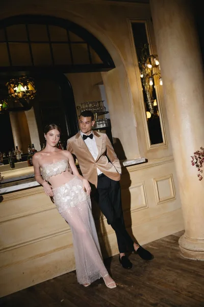 Couple portrait of bride and groom at bar, she in a two piece wedding dress with sheer skirt, he in a velvet tux jacket.