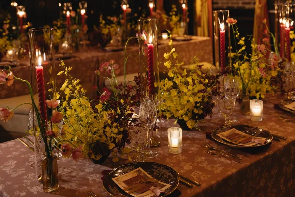 Reception tablescape at a candlelit wedding table featuring crystal glassware, framed by a brick fireplace and dark walls in an indoor dining room.
