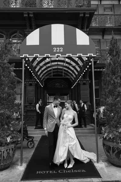 Couple portrait, a classic hotel wedding portrait under a striped awning at the hotel entrance, the bride holding a bouquet amid string lights.