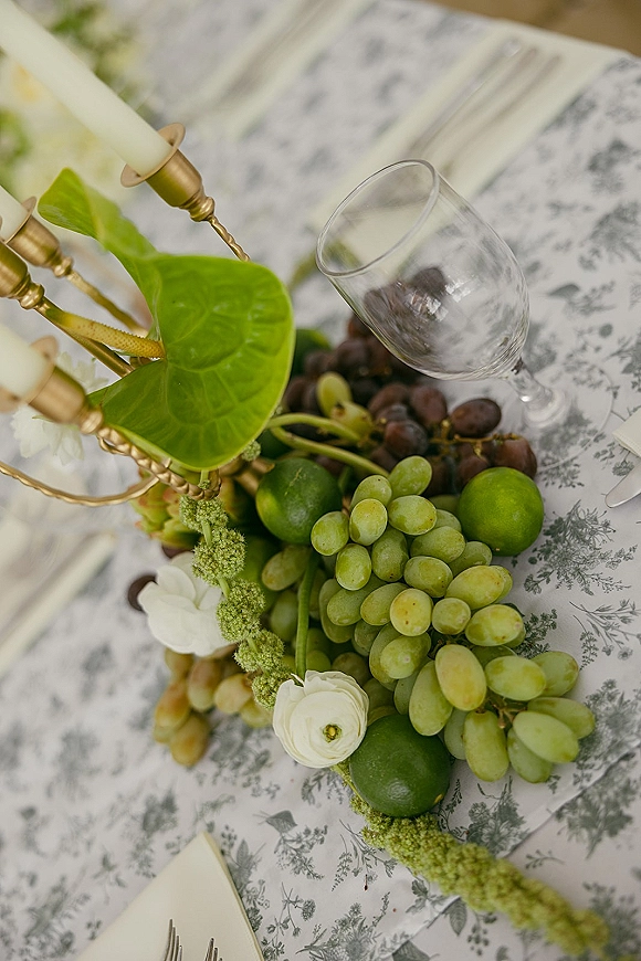 Reception tablescape with green and white tablescape styling, brass candelabra and taper candles, grapes, limes, and botanical linens