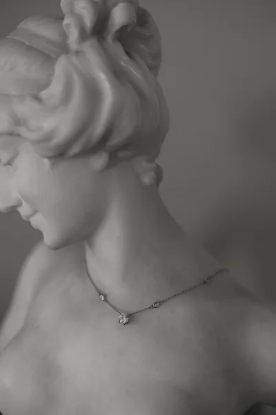 Bridal jewelry with a diamond pendant necklace on a bride’s collarbone, chain resting above a low updo against a plain wall