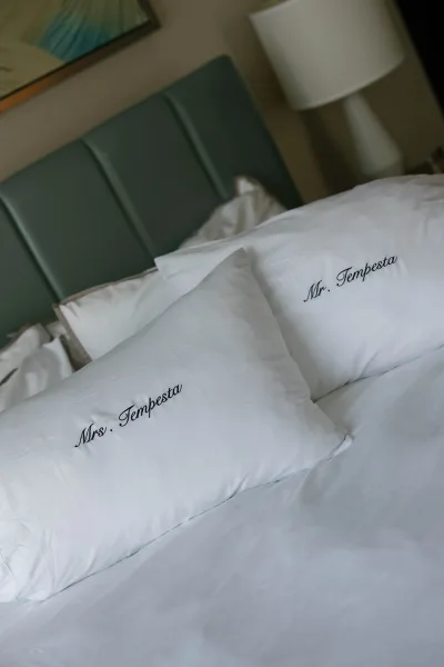 Wedding monogram pillows with mr and mrs pillowcases embroidered in script on a hotel bed, framed by crisp linens and a bedside lamp