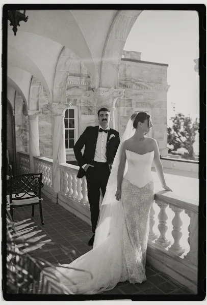 Couple portrait in a black and white wedding portrait style, bride in lace gown and cathedral veil beside groom in tux under arched colonnade