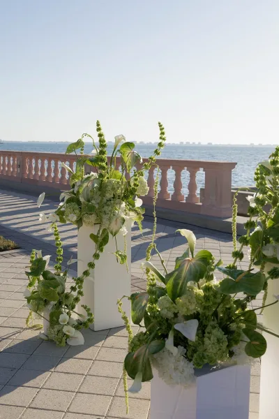 Ceremony aisle florals with wedding aisle flower pillars on white pedestals, calla lilies and trailing greenery on a waterfront terrace