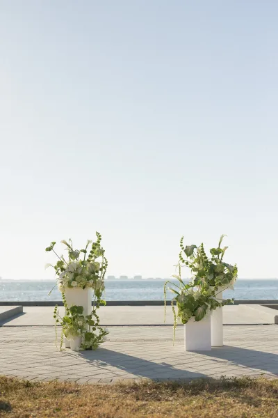 Ceremony altar decor with modern wedding altar white pedestal plinths, calla lilies and trailing greenery on a terrace overlooking the ocean horizon