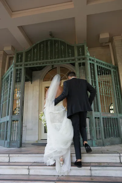 Couple portrait of bride and groom walking away up stone steps, her long veil and lace dress trailing as they enter an arched doorway