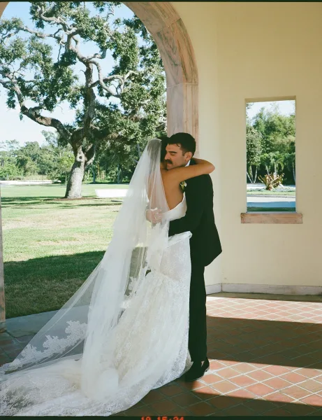 Wedding couple portrait of bride and groom embrace, her long cathedral veil trailing on terracotta tiles beneath a villa archway