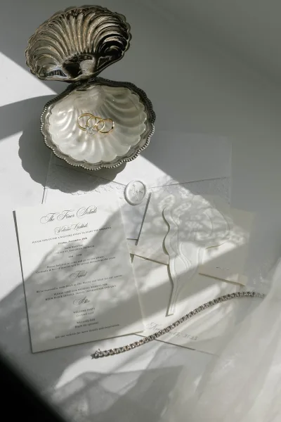 Invitation suite wedding invitation flatlay with rings in a pearl shell box, wax seal and ribbon on white fabric with sunlit shadows