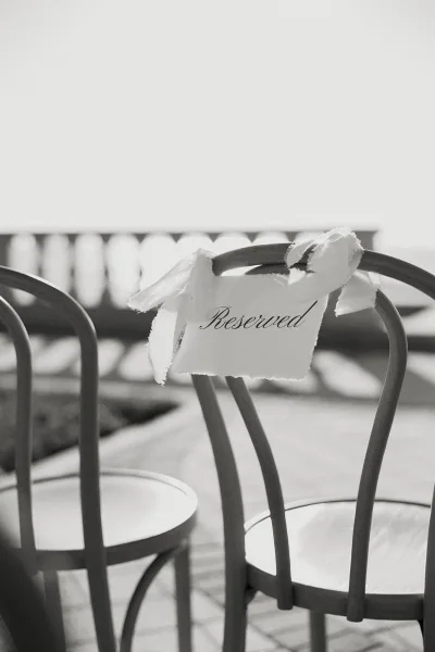 Reserved seat sign with calligraphy on a deckle-edge card tied with a white ribbon to a chair in warm patio sunlight