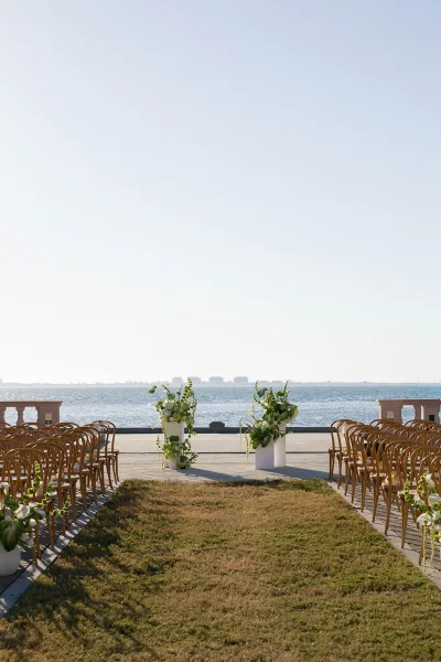 Ceremony setup with outdoor ceremony chairs and a wedding aisle runner, lined with white florals and greenery on a seaside terrace with ocean horizon