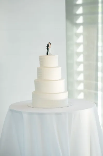 Wedding cake with four tier wedding cake design, smooth white buttercream and bride-and-groom topper on a round table in window light
