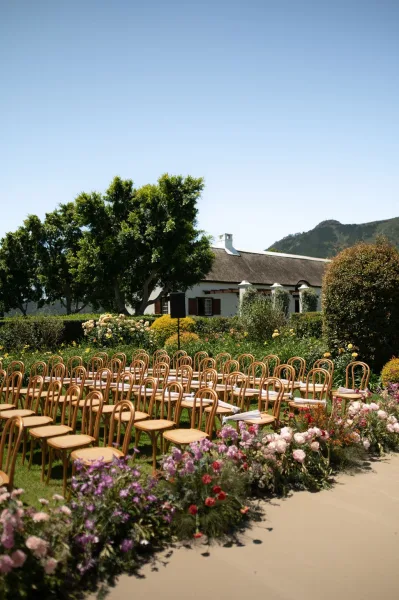 Garden ceremony setup with outdoor ceremony seating in bentwood chairs on a grass lawn, framed by garden trees and distant mountains.