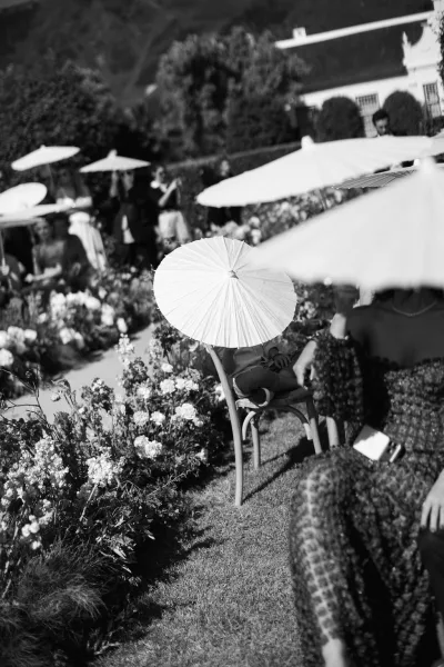 Outdoor ceremony setup with garden ceremony seating and paper parasols on a lawn, framed by neat hedges and a distant mountain backdrop.