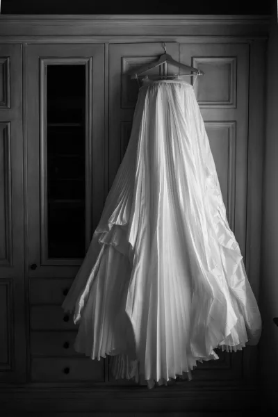 Wedding dress hanging on a wooden hanger against a wood armoire with wardrobe doors in an indoor room, centered on the wardrobe panels.