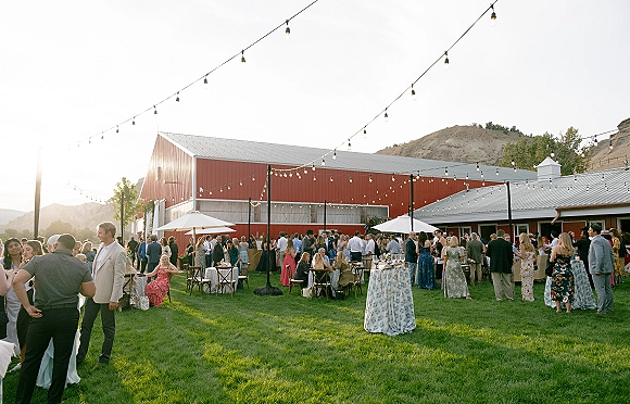 Outdoor wedding reception with barn wedding reception ambiance, high top cocktail tables under string lights by a red barn with mountains beyond