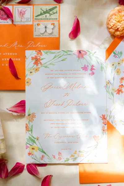 Wedding invitation suite with floral wedding invitation, envelopes, stamps, and wax seal on linen fabric with sunlit shadows and petals