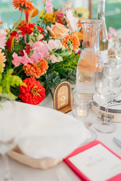 Reception tablescape with wedding table centerpiece of colorful wedding flowers, table number sign, wine glasses, votive candle on white linen tablecloth