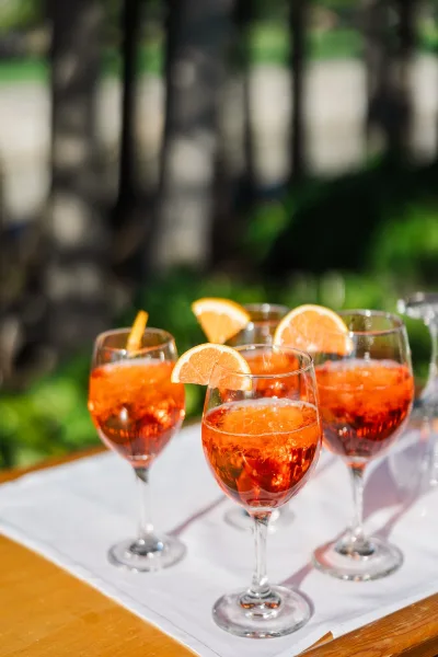 Wedding welcome drinks with aperol spritz wedding cocktails in wine glasses on a wooden tray, orange slice garnish glowing in sunlight outdoors