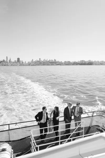 Boat wedding guests mingle with cocktails on the open deck, inspiring yacht wedding ideas as the city skyline rises beyond the water's wake.