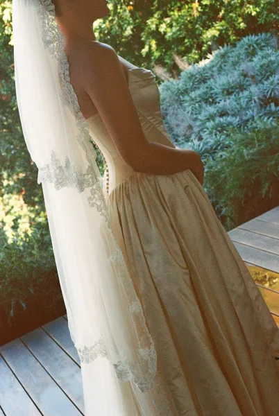 Wedding dress close up of a strapless wedding dress with covered buttons, framed by shaded garden foliage and a wooden deck.