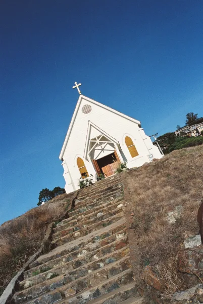 Church wedding venue showcasing a charming chapel exterior with stone steps, set against a blue sky and dry grass hillside