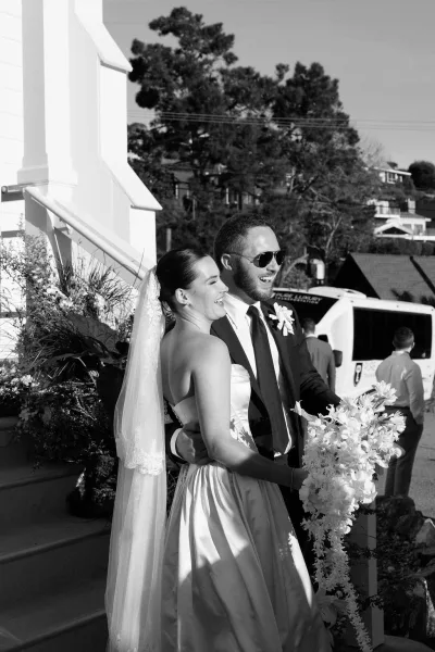 Couple portrait of a bride and groom smiling, she holds a cascading orchid bouquet, their elegant just married moment captured in classic style.