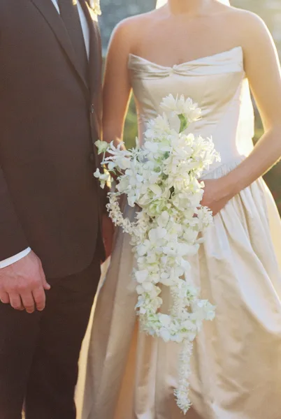 Cascading bouquet, a white orchid bouquet, held by the bride with a soft veil, trailing blooms against sunlit garden greenery.