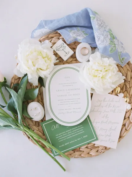 Invitation suite wedding invitation flat lay with arched cards, rings, pearl earrings, peonies, and blue floral scarf on a white surface