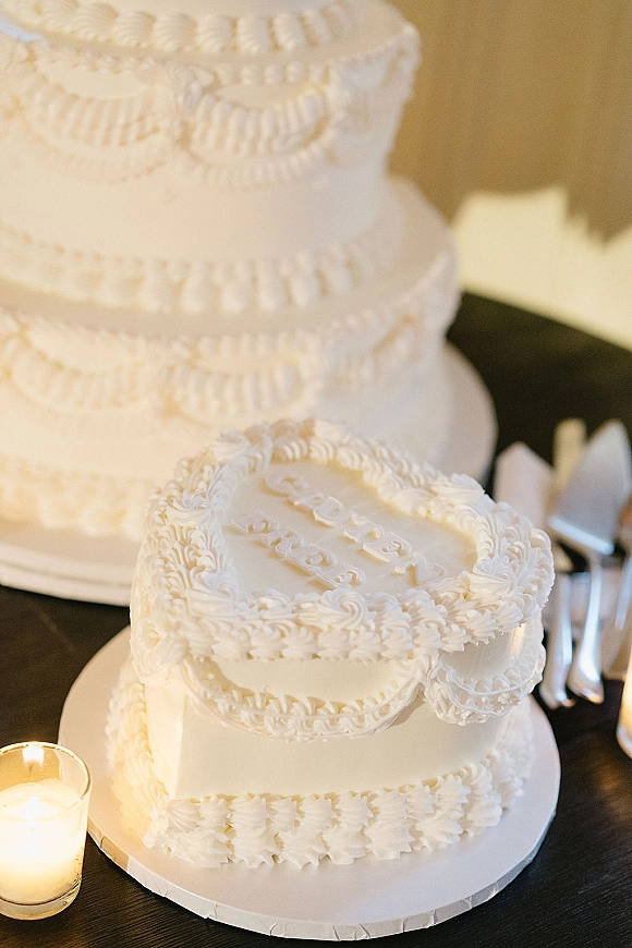 Wedding cake with white buttercream wedding cake ruffled piping on a dark wood table, with cake knife, server, and candlelight in votive