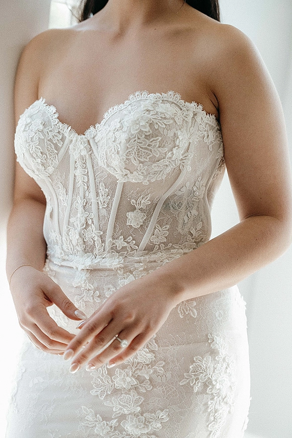Wedding dress close-up showing strapless lace wedding dress with sheer boned corset bodice and engagement ring in soft indoor light