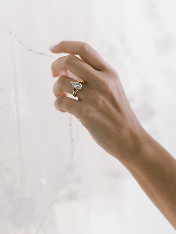 Engagement ring with a pear cut diamond in a gold setting, photographed close up against a sheer veil on a white background