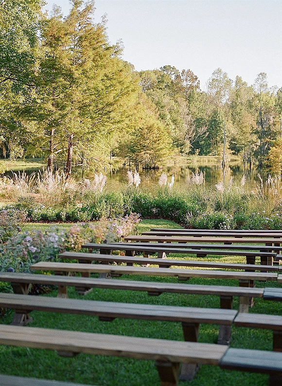 Ceremony seating with outdoor wedding ceremony seating on wood benches arranged in rows on a lawn, facing a lakeside backdrop of trees and sky