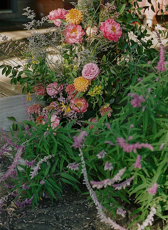 Wedding floral arrangement with ceremony ground flowers in pink and yellow wildflowers and greenery spilling over wooden steps in a garden setting