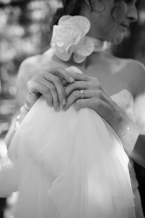 Bridal ring close-up showing an engagement ring close up and wedding band on the bride’s finger as she holds her veil, greenery bokeh behind