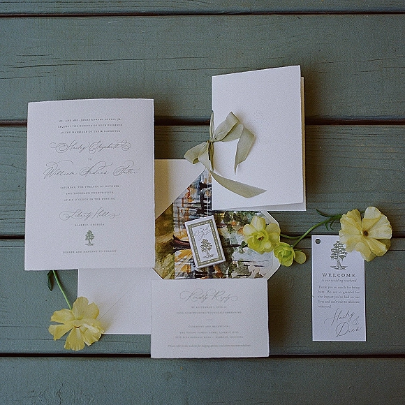 Invitation suite wedding invitation set arranged with envelope, RSVP and details cards, green ribbon bow, wax seal and yellow flowers on painted wood surface