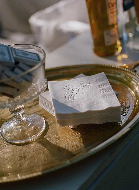Wedding cocktail napkins and custom wedding napkins stacked on a brass tray beside a crystal candy dish and chocolate bars on a reception table