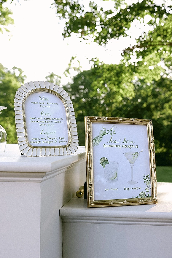 Bar signage with a wedding bar sign in gold frames, featuring calligraphy cocktail illustrations on a white bar counter in garden greenery