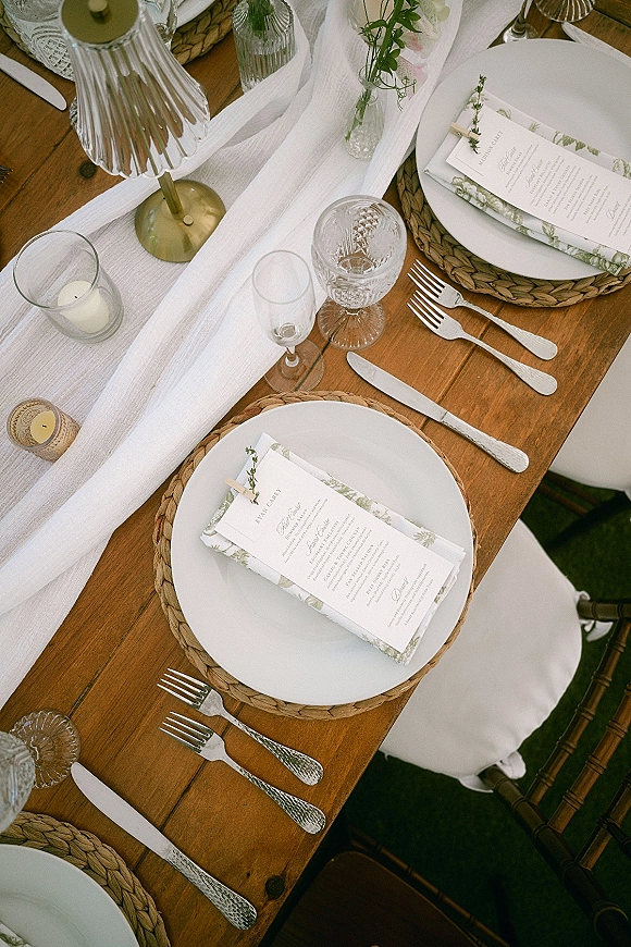 Reception tablescape with rustic wedding tablescape details, rattan chargers, white plates, gauze runner, brass lamp, and votive candles on a lawn