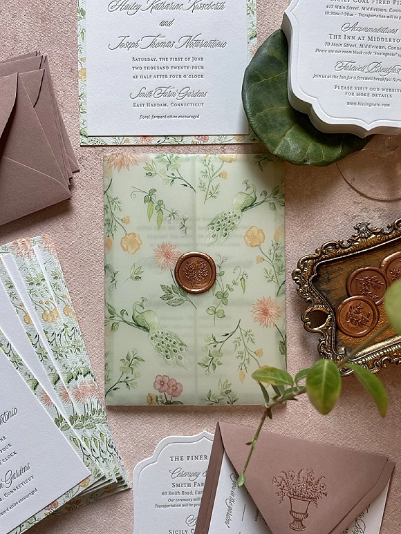 Wedding invitation suite with floral wedding invitations, blush envelopes, vellum wrap and wax seal on an ornate brass tray over pink fabric backdrop