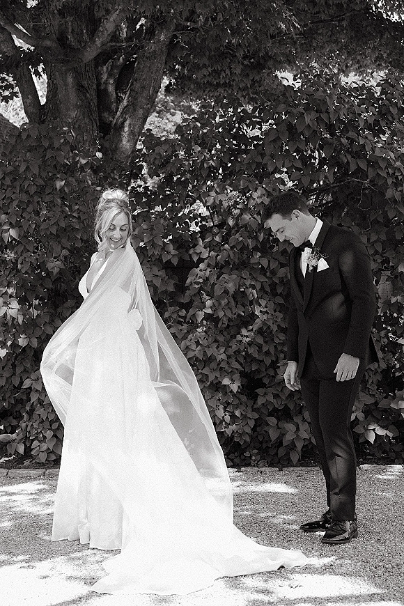 Couple portrait in a black and white wedding portrait style, bride in strapless gown with long veil and groom in tux on a garden path