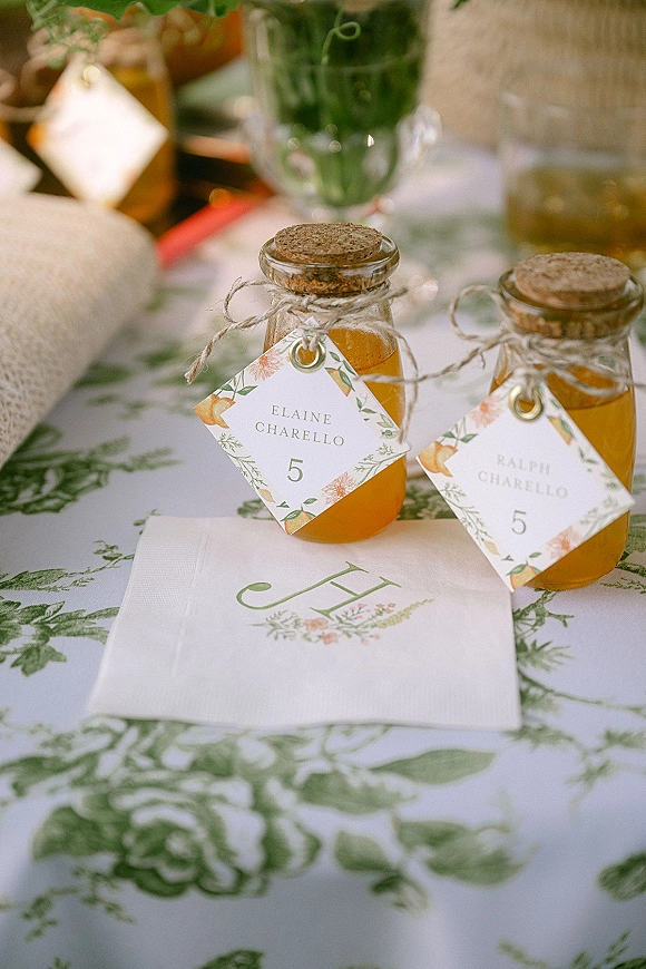 Wedding place cards with mini glass bottles and cork stoppers, twine-tied hang tags, and floral border stationery on a patterned table setting