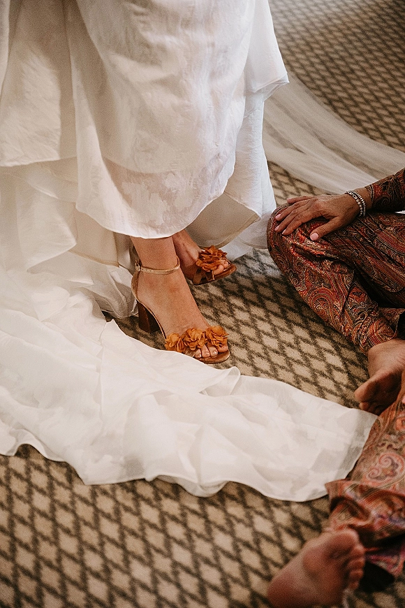 Bridal shoes with floral appliques, wedding shoe detail showing ankle-strap heels under a white dress train on patterned carpet