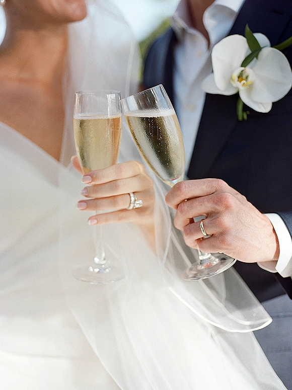 Wedding champagne toast with bride and groom toasting in close-up, hands showing rings and champagne flutes in soft light background