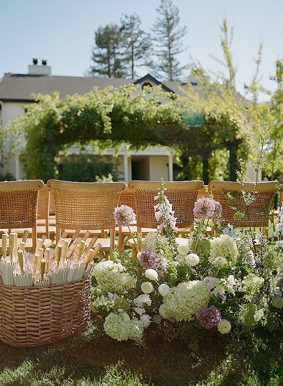 Ceremony seating with outdoor wedding ceremony chairs in neat rows, cane backs facing a pergola, with hydrangea aisle flowers and ribbon wands