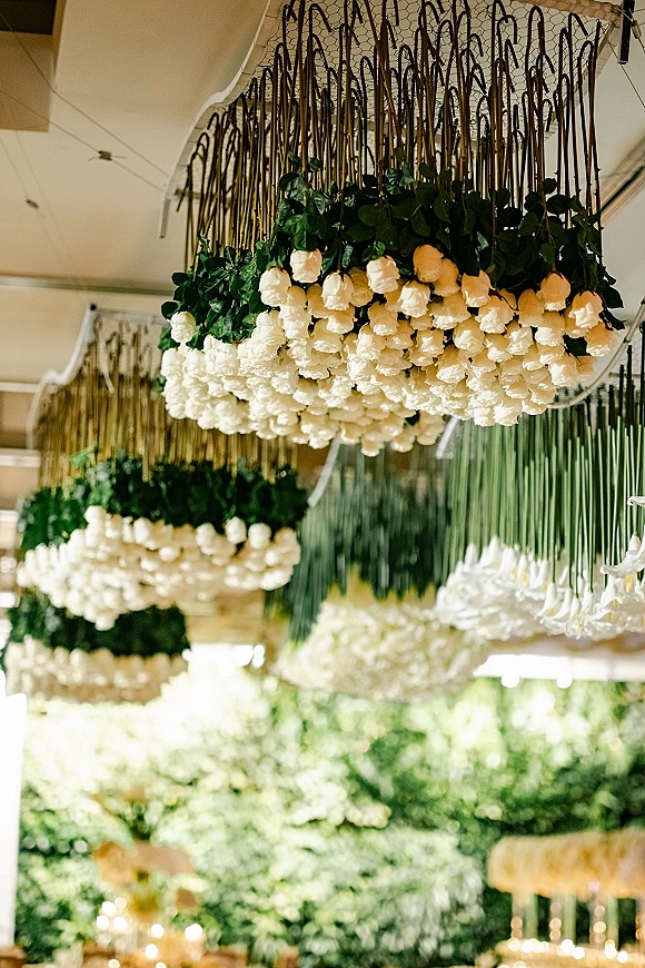 Hanging floral installation with white roses and greenery suspended from chicken wire, creating a floral chandelier wedding ceiling above reception space