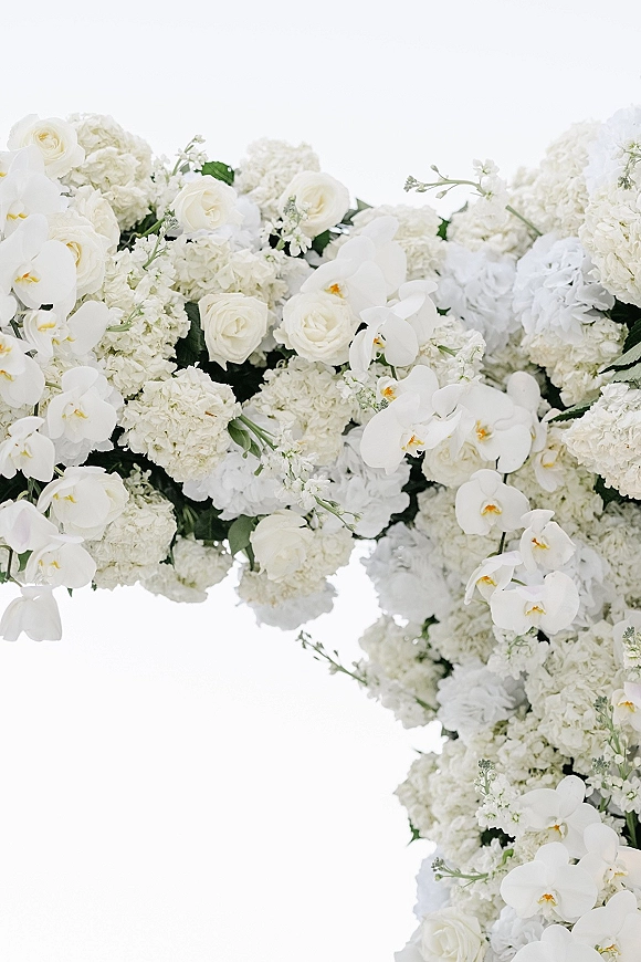 Wedding floral arch with white roses, orchids, and hydrangeas with greenery accents against a clean white backdrop
