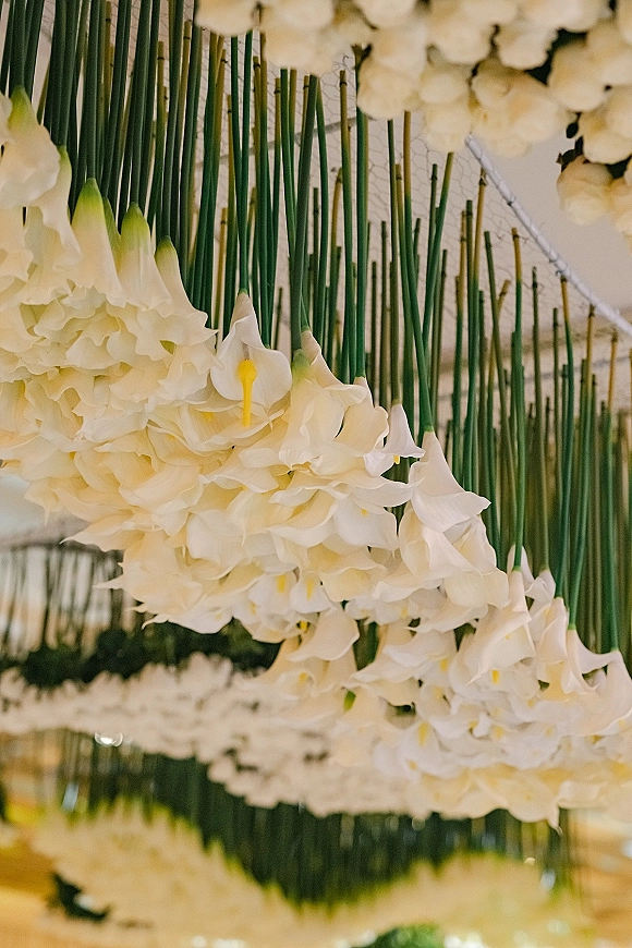 Floral ceiling installation with hanging calla lilies and suspended greenery forming a modern overhead canopy against an indoor ceiling structure